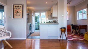 A modern kitchen with white cabinets, a central island, and a dining area with a yellow chair and a red cabinet. - Sunny, Character 2 Bedroom Home - Mission Bay (Auckland)