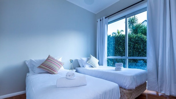 A hotel room with two beds, white bedding, a window with curtains, and a view of greenery outside. - Sunny, Character 2 Bedroom Home - Mission Bay (Auckland)