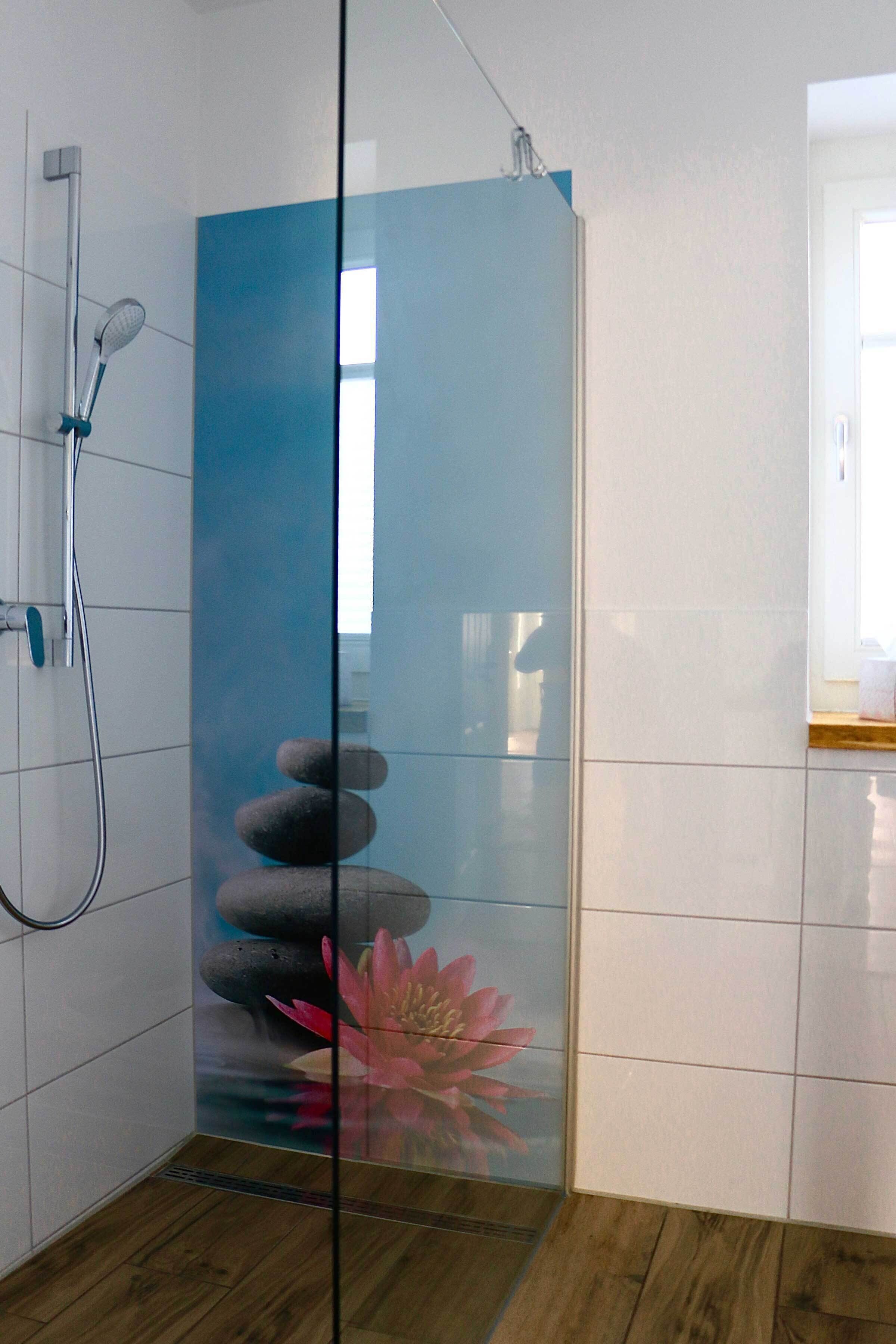 Un baño moderno con cabina de ducha de vidrio, paredes de azulejos blancos y suelo de madera.