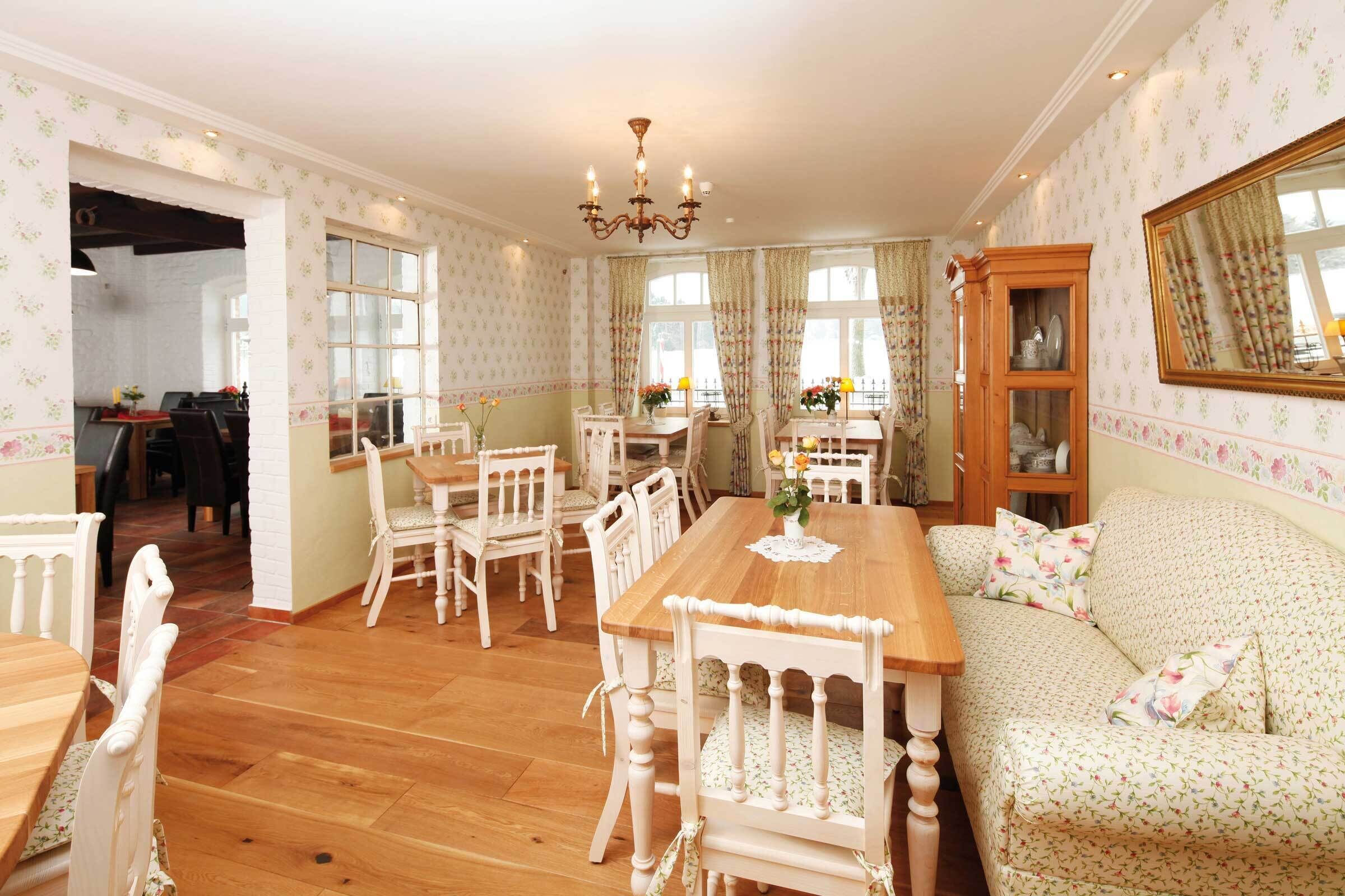 A dining area with a wooden table and white chairs, a sofa with floral upholstery, and a chandelier.