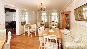 A dining area with a wooden table and white chairs, a sofa with floral upholstery, and a chandelier.