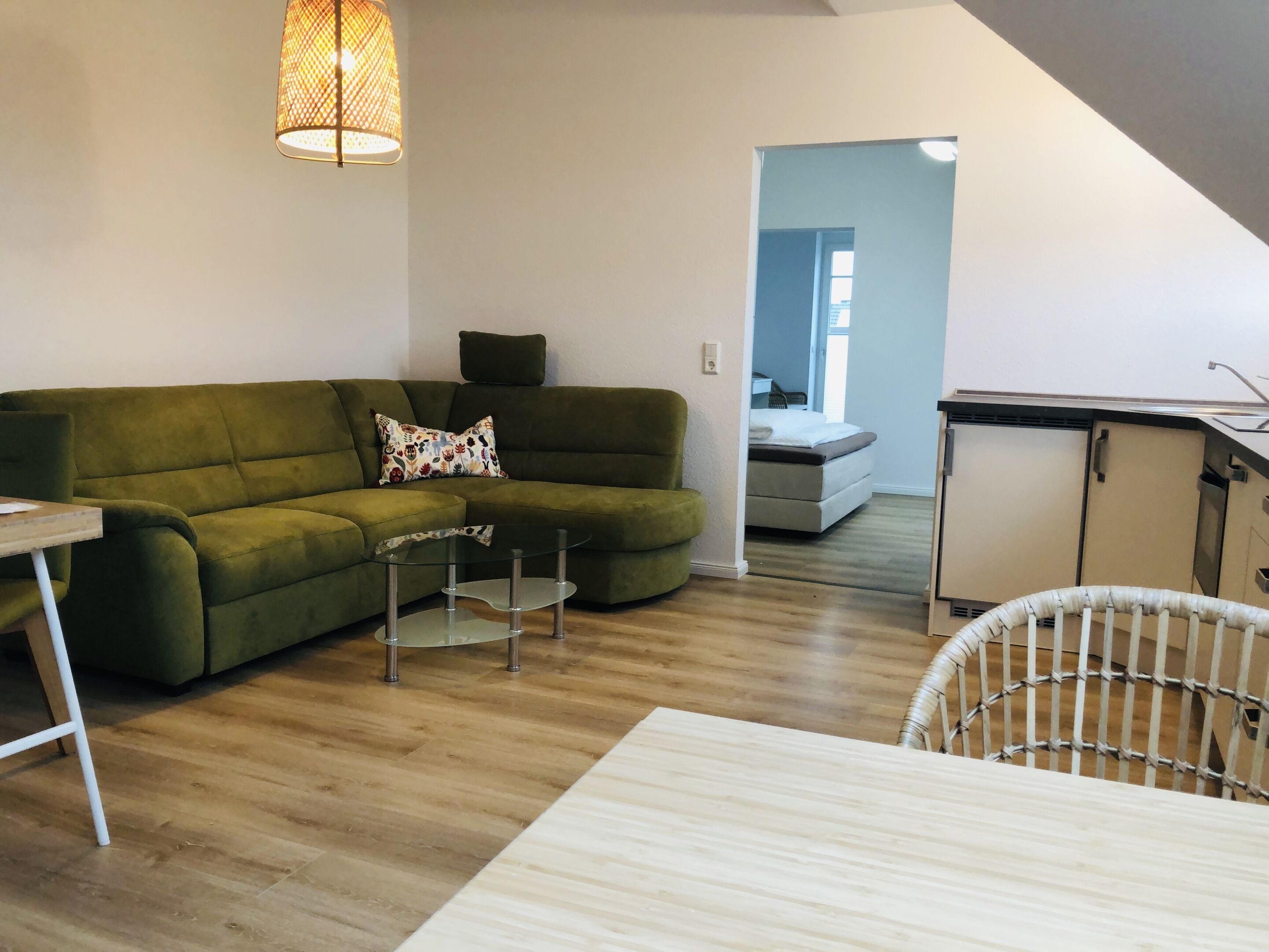 Una sala de estar con un sofá verde, una mesa de centro de vidrio, una silla de mimbre y una cuna blanca.