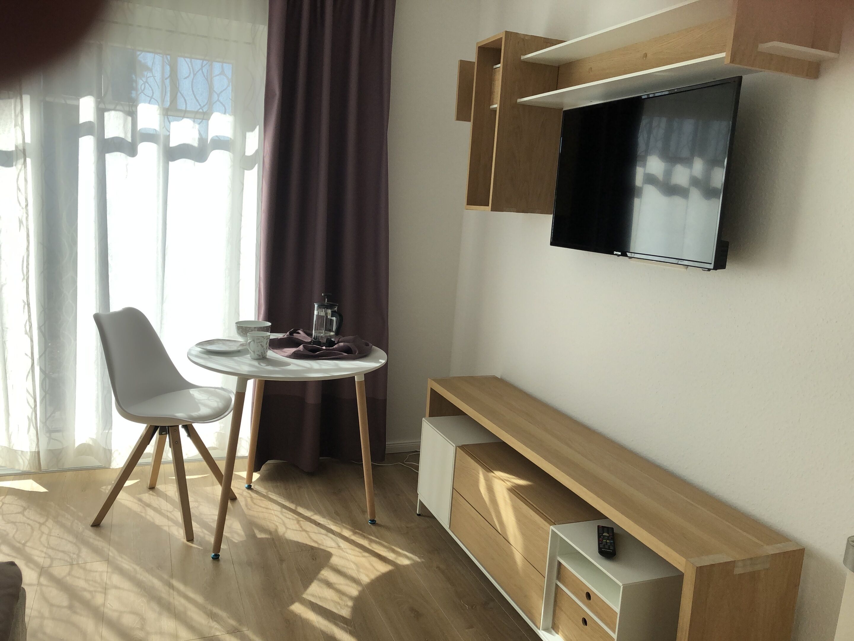 Un salon moderne avec un téléviseur fixé au mur, une table à manger ronde avec une chaise, et un banc en bois intégré doté de tiroirs de rangement.