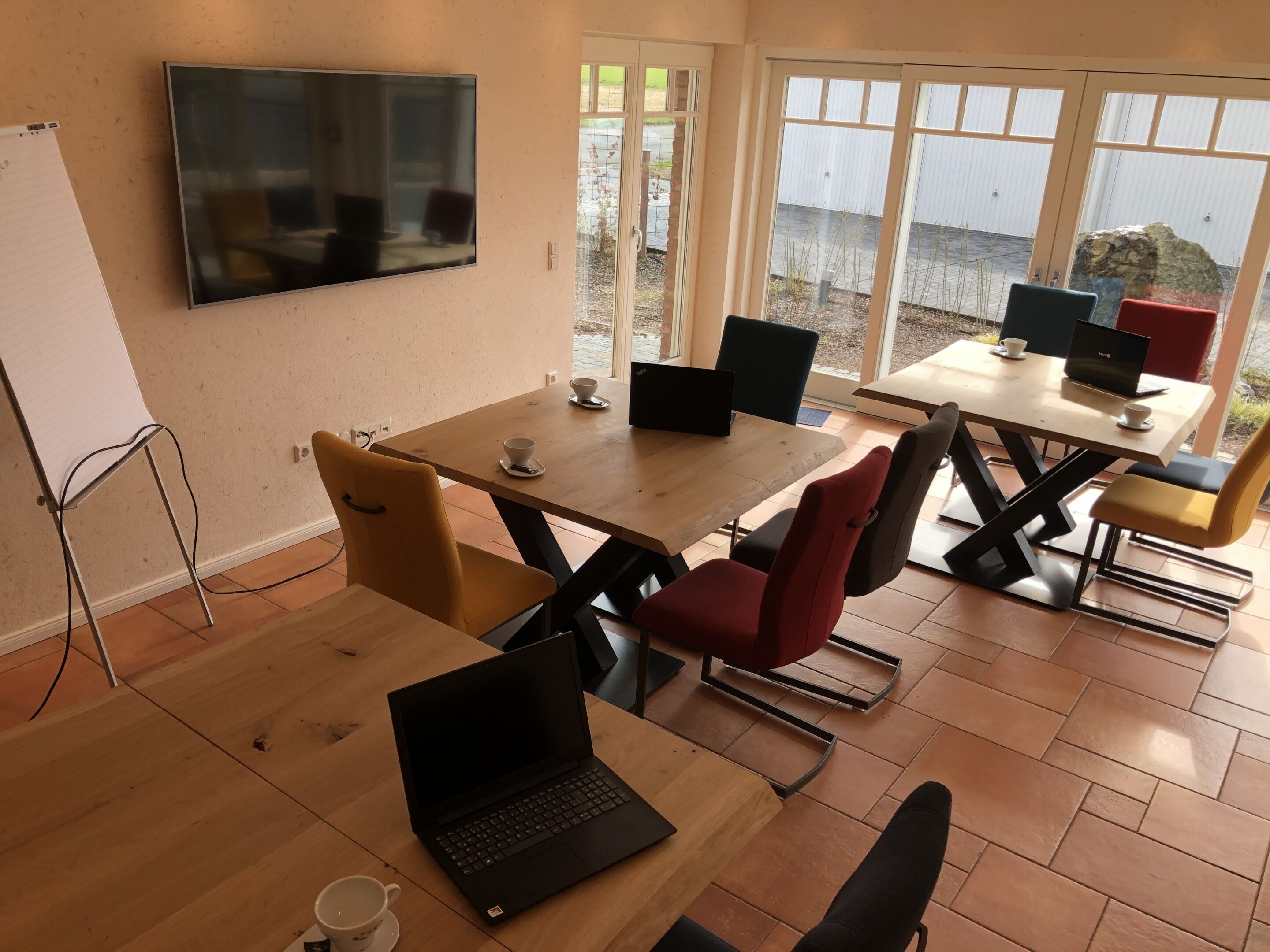 A modern meeting room with a large TV, multiple laptops, and a whiteboard.