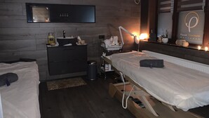 Une chambre avec deux lits, une coiffeuse avec un miroir, une table de chevet, un climatiseur mural et un panneau indiquant « Pause Thermale Bien-être ».