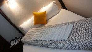 Una cama bien hecha con ropa de cama estampada, una almohada amarilla y una almohada blanca.