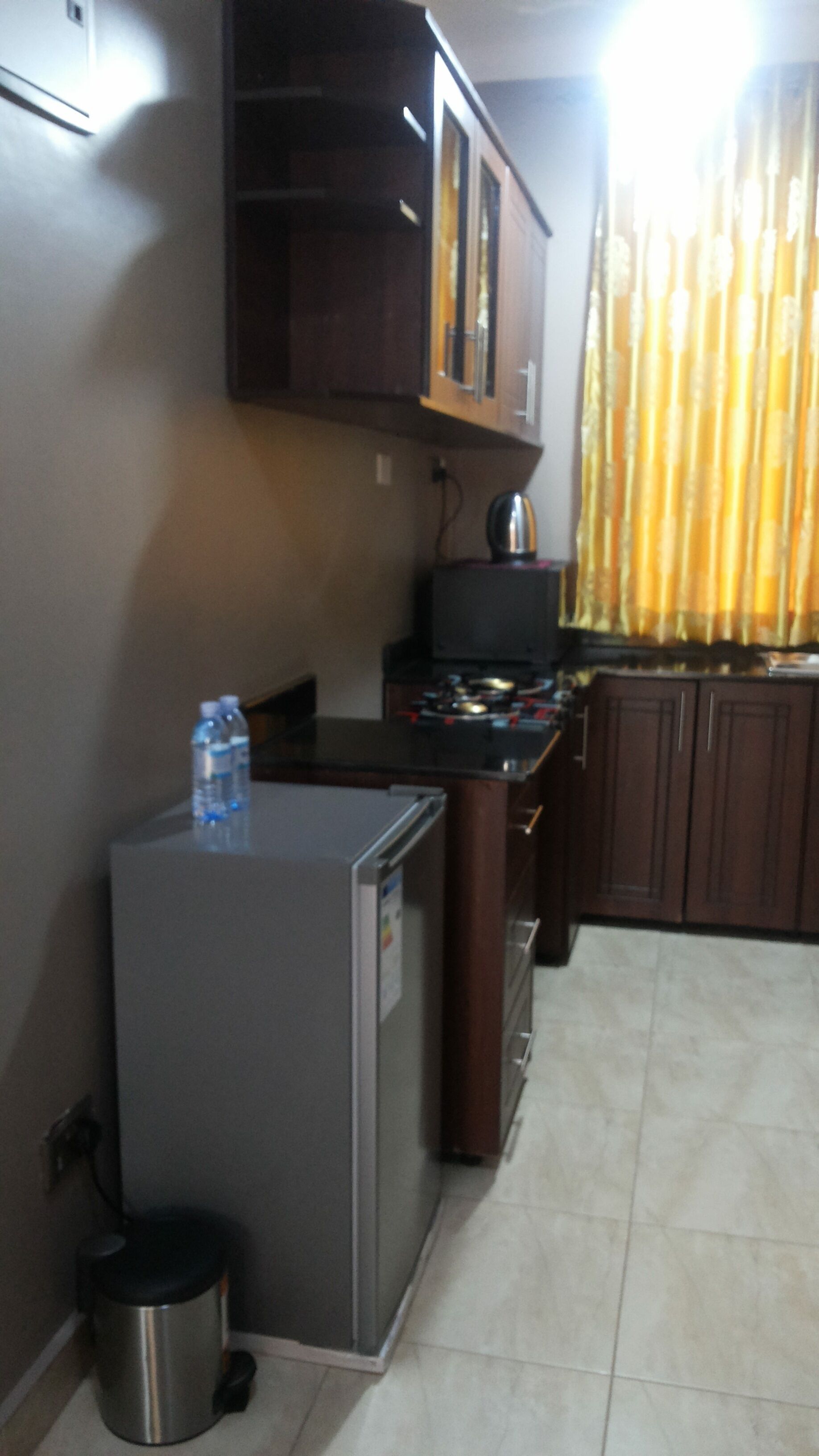 Una cocina compacta equipada con refrigerador, dispensador de agua, hervidor y un pequeño bote de basura.