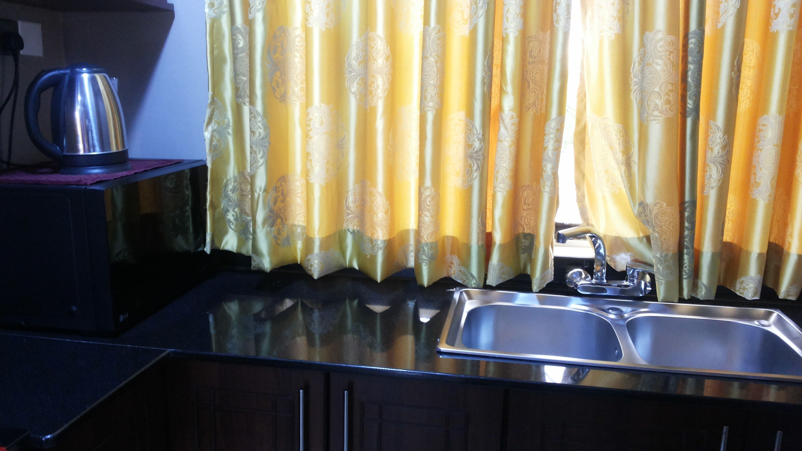 Uma cozinha com pia de aço inoxidável, chaleira e cortinas amarelas com padrão.