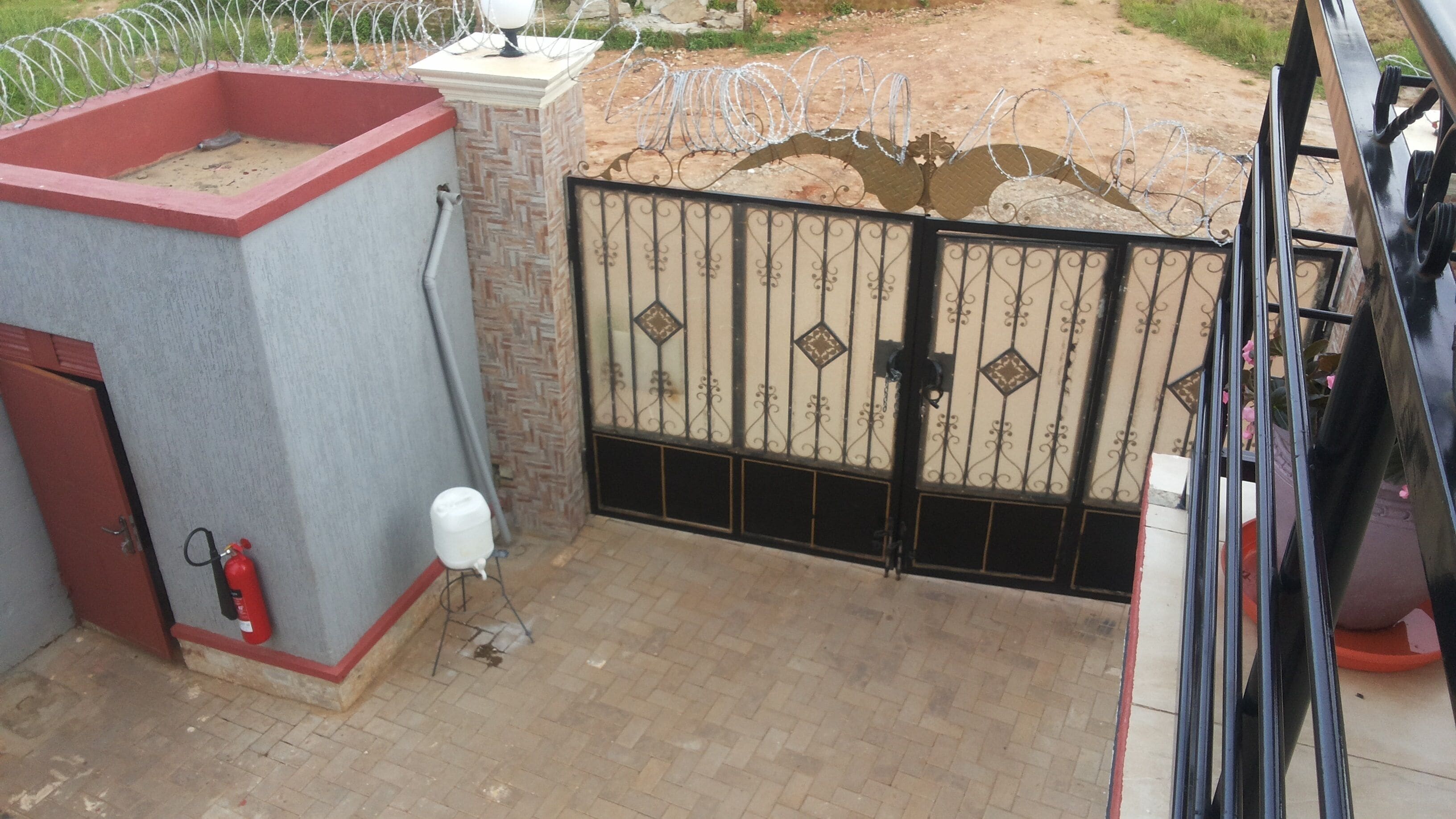 A gated entrance with a metal gate, a fire extinguisher, and a water dispenser on the left.