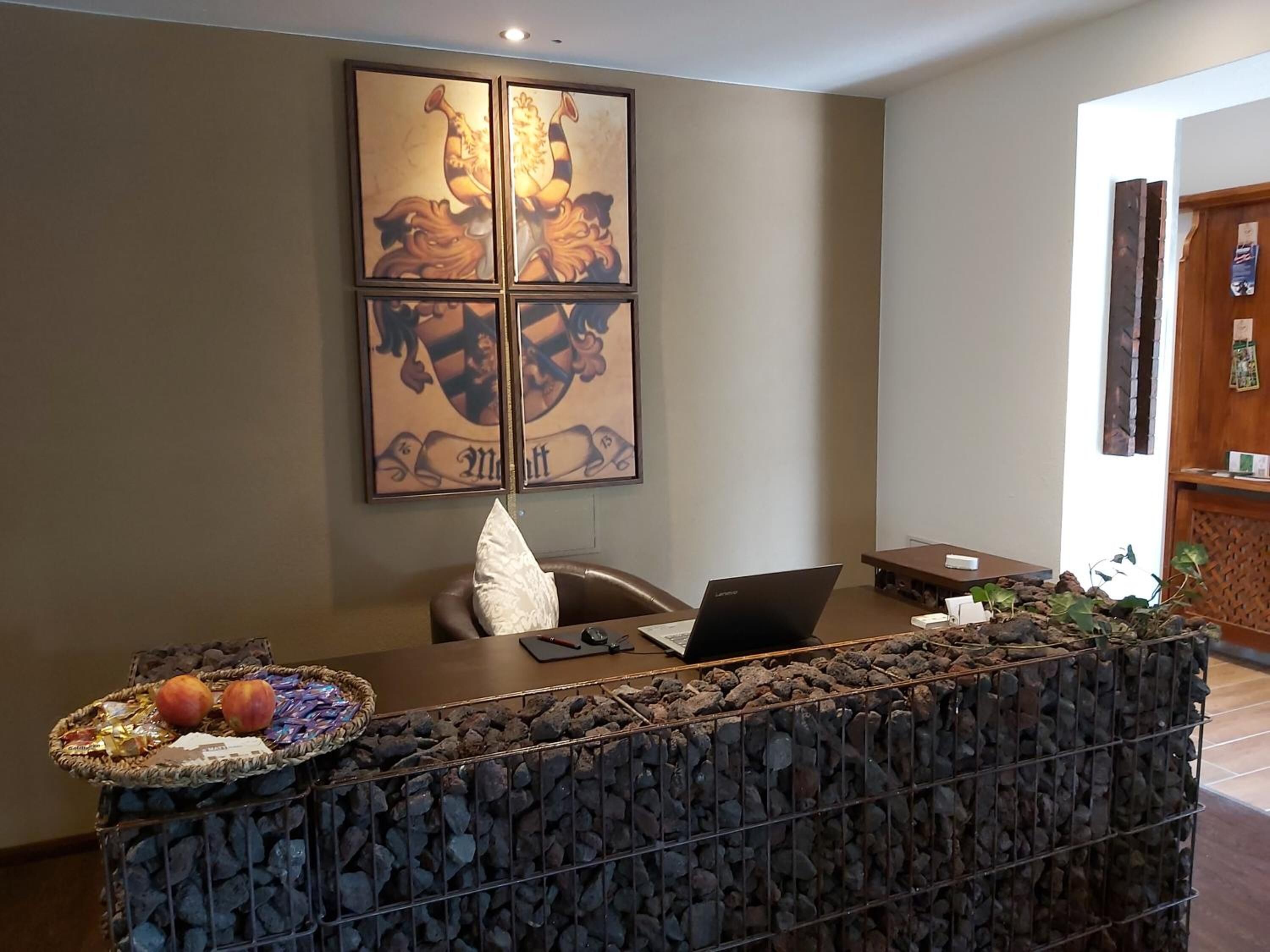 Bancada de recepção com um laptop, uma cesta de frutas e um objeto decorativo na parede.