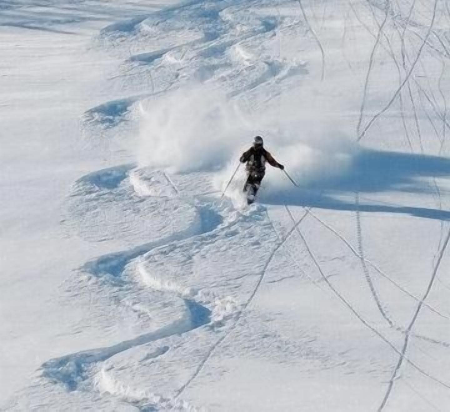 Eine Person fährt auf Skiern einen verschneiten Hang hinunter, deutliche Spuren sind im Schnee zu sehen.