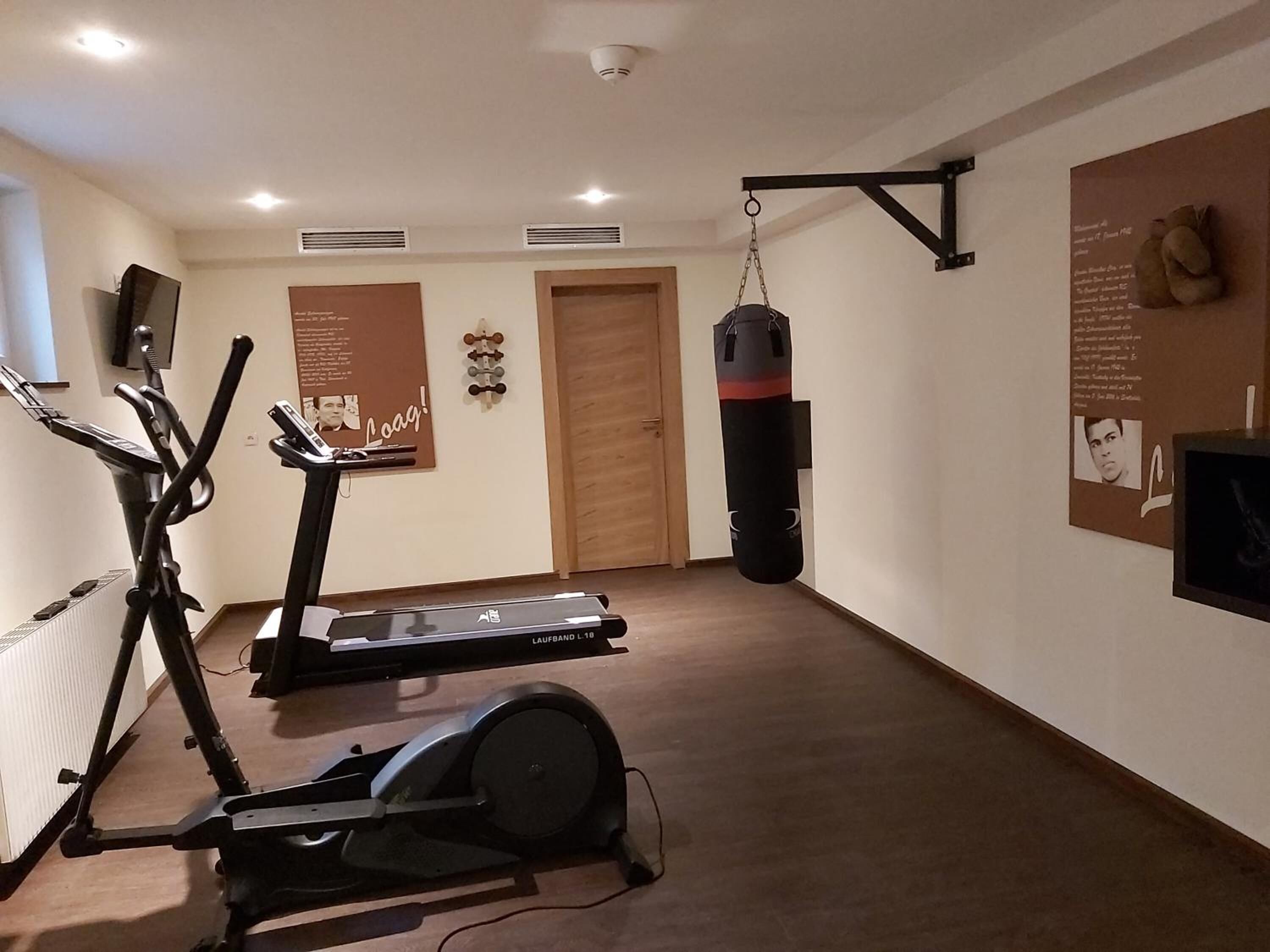 Ein Fitnessraum mit Cardiogeräten, einem Boxsack und einer Wand mit Motivationspostern.