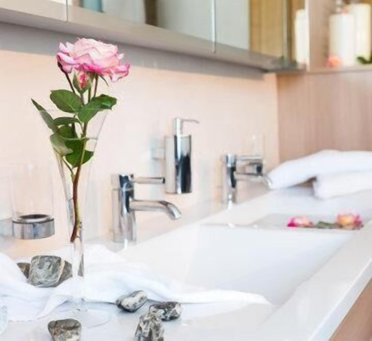 Ein Badezimmer mit einem weißen Waschbecken, einer Rose in einer Vase und einem Handtuchhalter.
