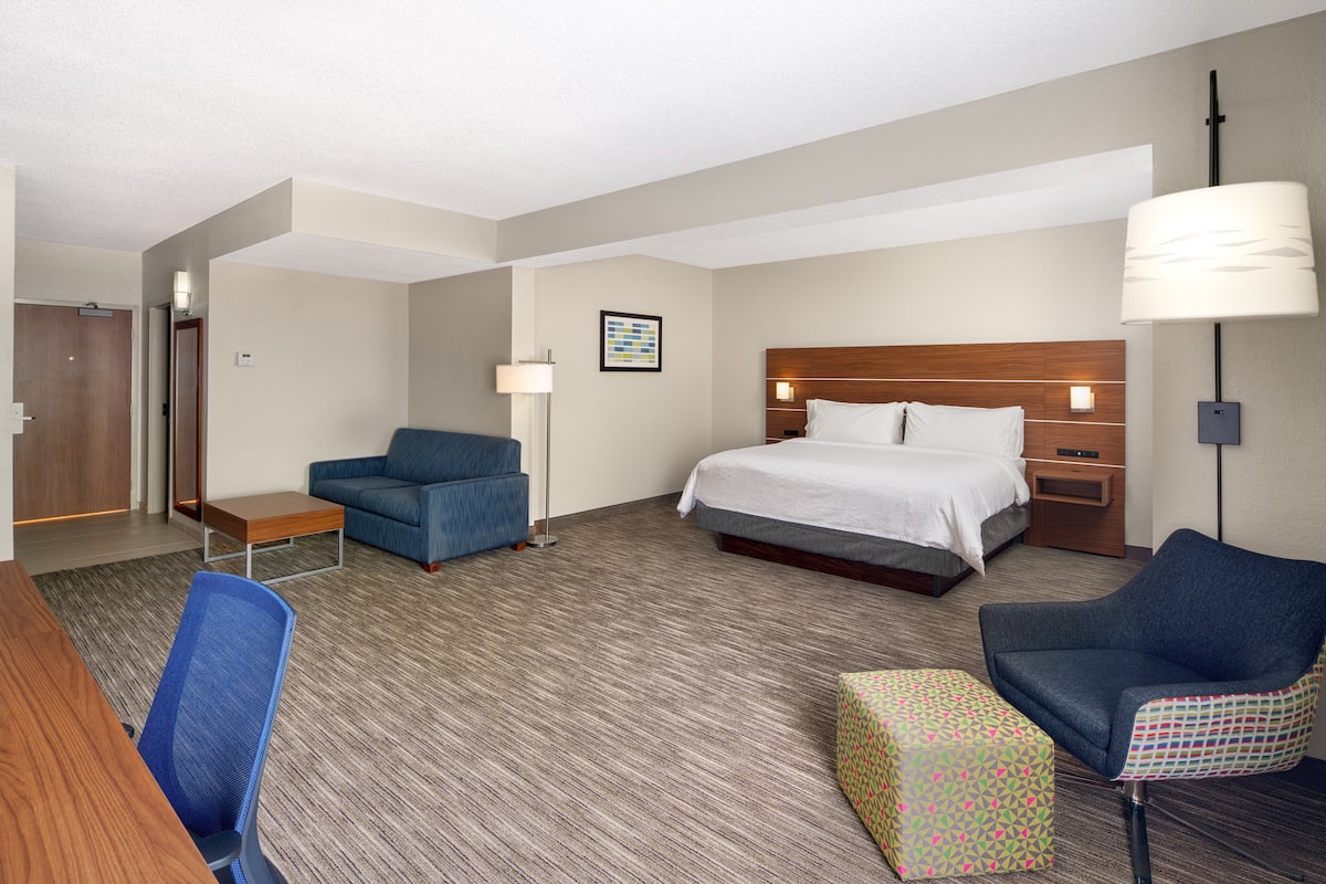 A hotel room with a bed, two chairs, a desk, a lamp, and a small table.