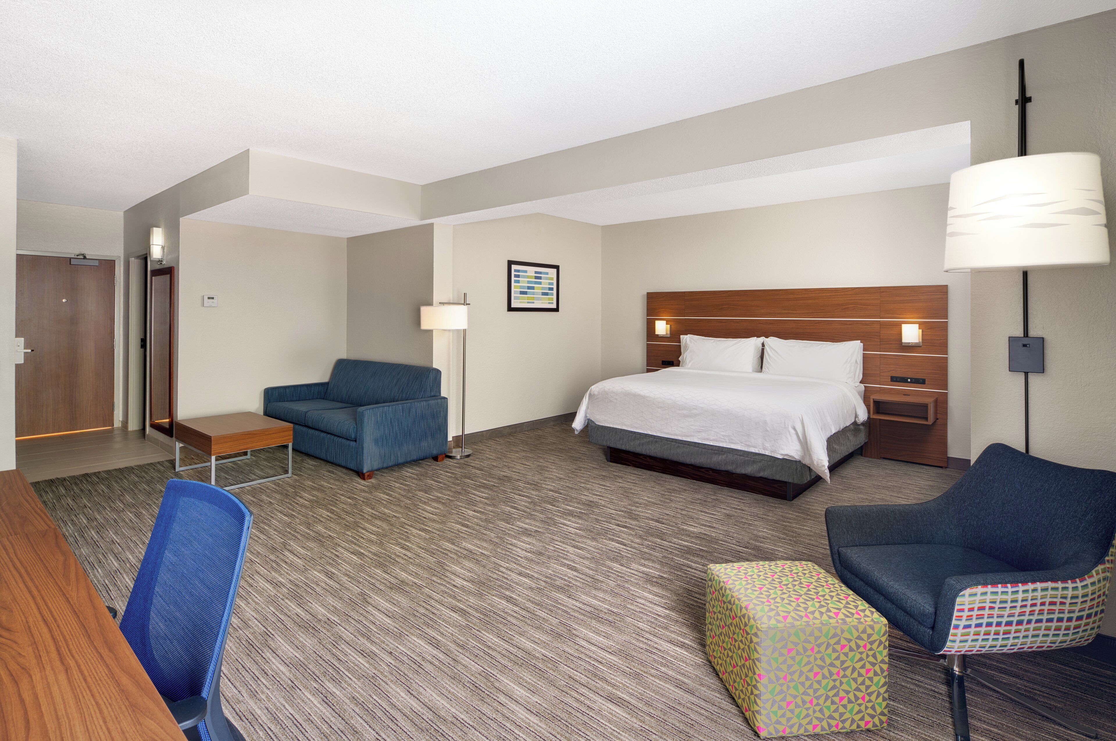 Quarto de hotel com cama, escrivaninha, cadeira, sofá, luminária e um quadro na parede.