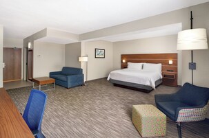 Quarto de hotel com cama, escrivaninha, cadeira, sofá, luminária e um quadro na parede.