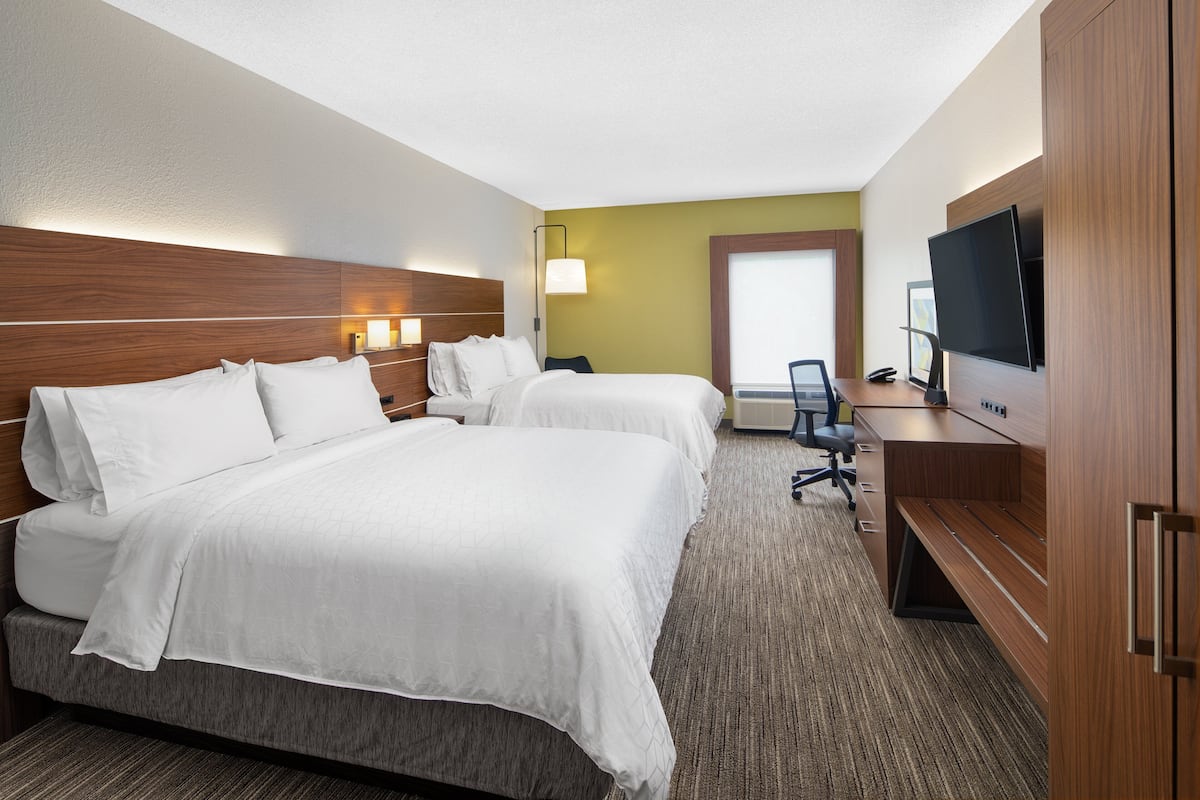 A hotel room with two beds, a desk, a television, and a large window.