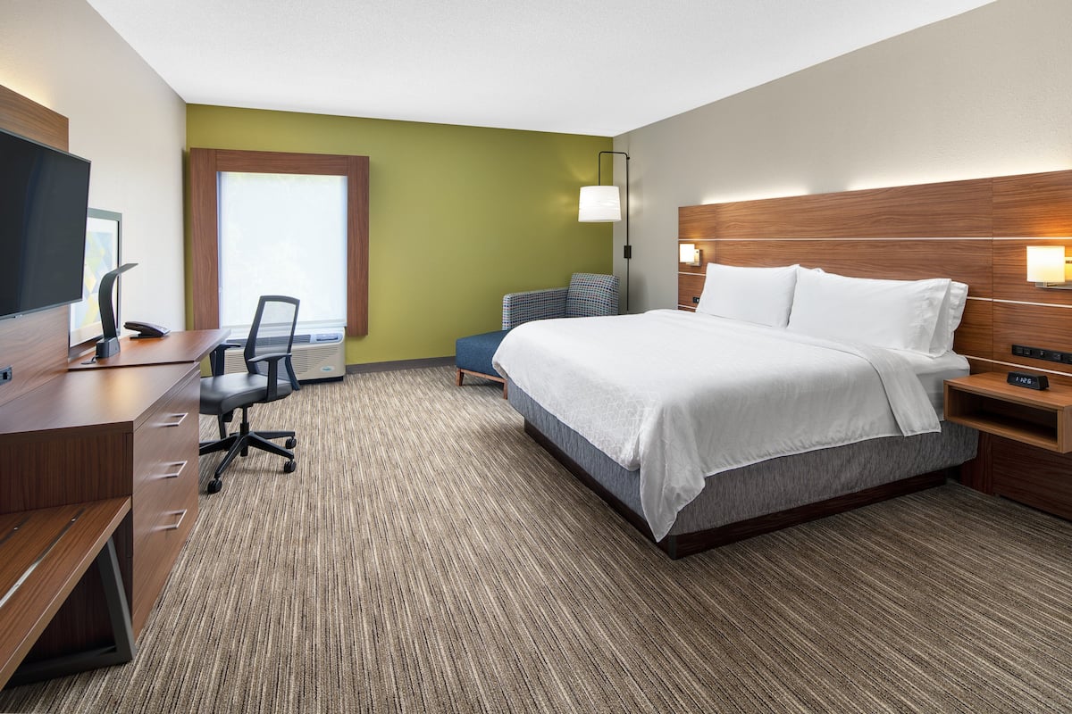 A hotel room with a bed, desk, chair, TV, and lamp.