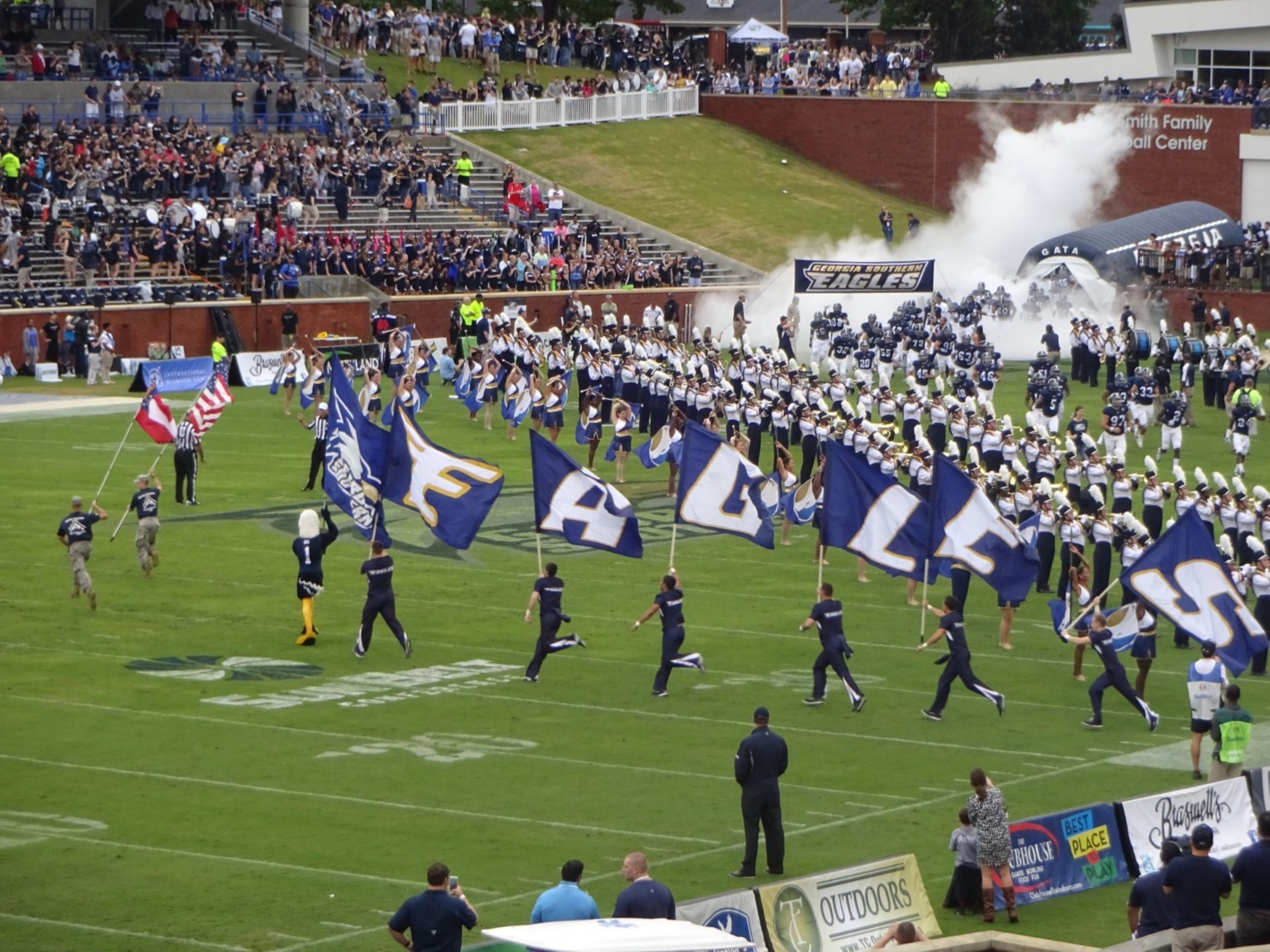 A marching band on a football field with spectators in the background.
