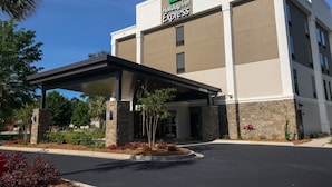 A Holiday Inn Express hotel with a covered entrance, stone pillars, and a landscaped area with red flowers. - Holiday Inn Express Statesboro by IHG (Statesboro)