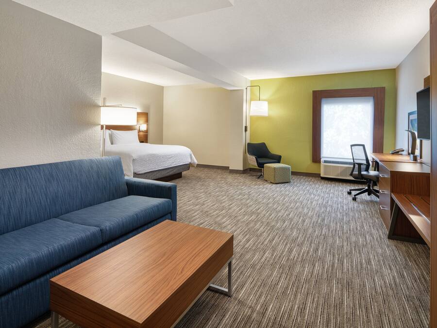 Quarto de hotel com uma cama, um sofá azul, uma mesa de madeira, uma escrivaninha, uma cadeira e um abajur.