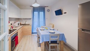 A compact kitchen with modern appliances, a dining table set for two, and a large window with blue curtains. - Elegant Pol's Loft  (Trieste)