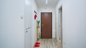 A narrow hallway with a wooden door at the end, a small plant on a pedestal, and a red mat on the floor. - Elegant Pol's Loft  (Trieste)