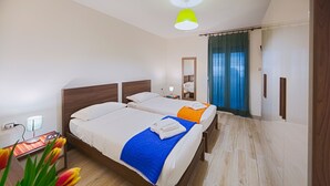 A hotel room with two beds, a nightstand with a lamp, a mirror, and a view of the outside through a window with curtains. - Elegant Pol's Loft  (Trieste)