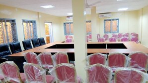 Une salle de conférence avec une longue table et de nombreuses chaises, dont certaines sont recouvertes de plastique.