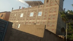 Un immeuble à plusieurs étages, doté d’une façade en briques, d’un toit plat avec des panneaux solaires et d’une petite structure en forme de tour située en haut à droite.