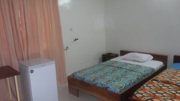 A bedroom with a single bed, a small bedside table, a nightstand, and a refrigerator.