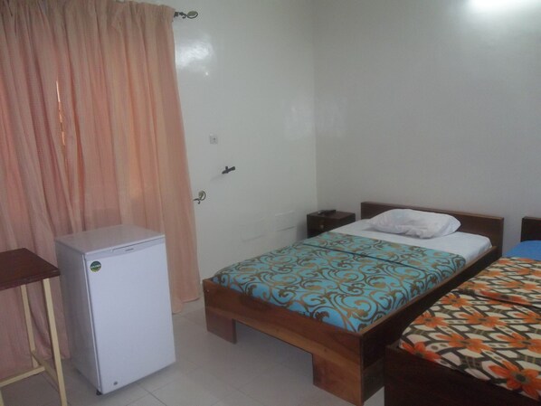A bedroom with a single bed, a small bedside table, a nightstand, and a refrigerator.
