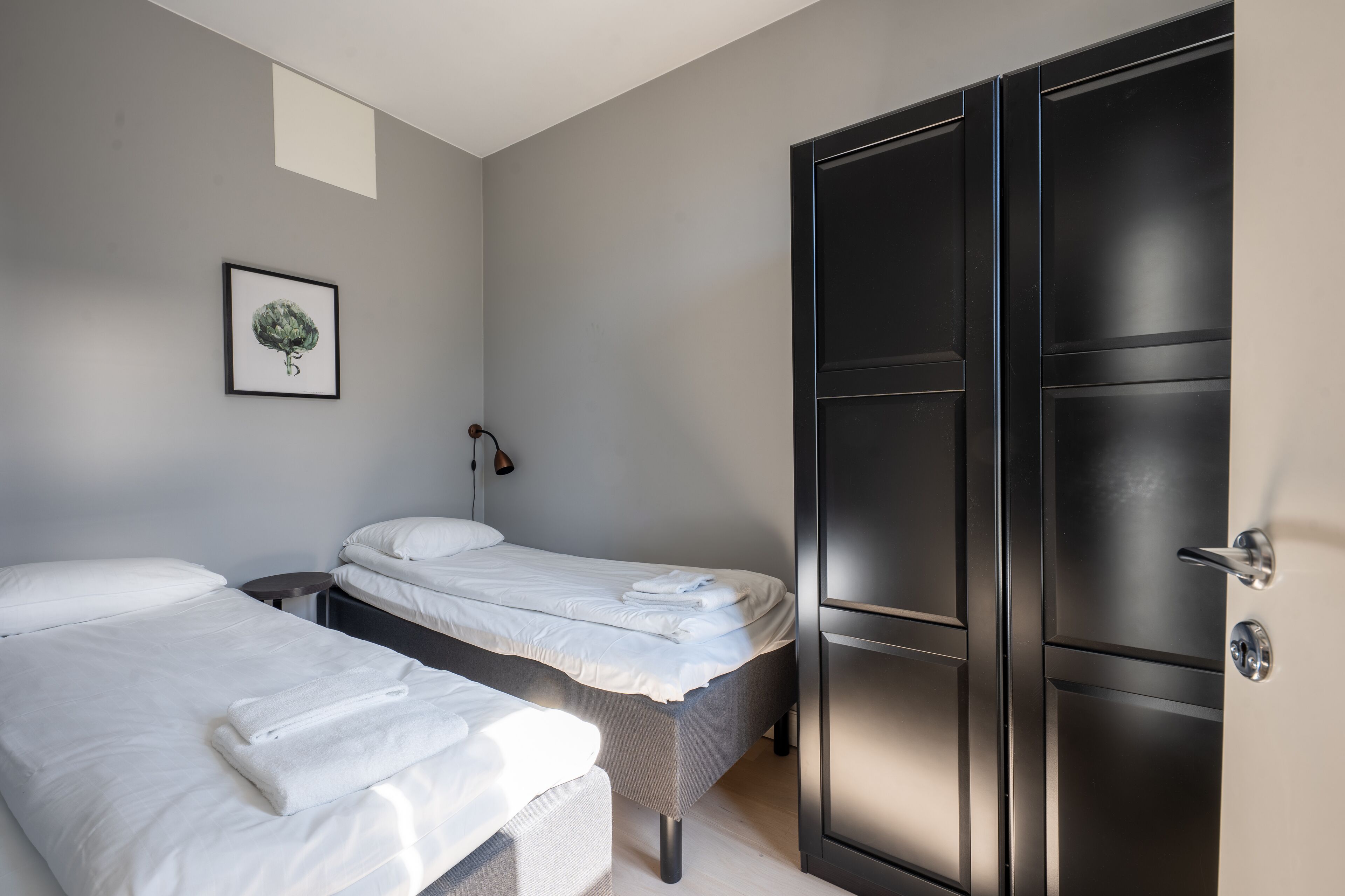 A hotel room with two beds, a wardrobe, a framed picture on the wall, and a small round table.