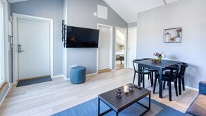 A modern living room with a flat-screen TV, a dining table with chairs, a blue ottoman, and a coffee table. - Forenom Serviced Apartments Schous Plass (Oslo)