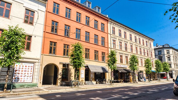 A street view with multi-story buildings, outdoor seating areas, and a clear blue sky. - Forenom Serviced Apartments Schous Plass (Oslo)