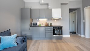 A modern kitchen with grey cabinets, a microwave, and an oven. There is a grey sofa with blue cushions in the adjacent living area. - Forenom Serviced Apartments Schous Plass (Oslo)