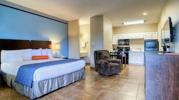A hotel room with a bed, a chair, a desk, and a kitchenette.