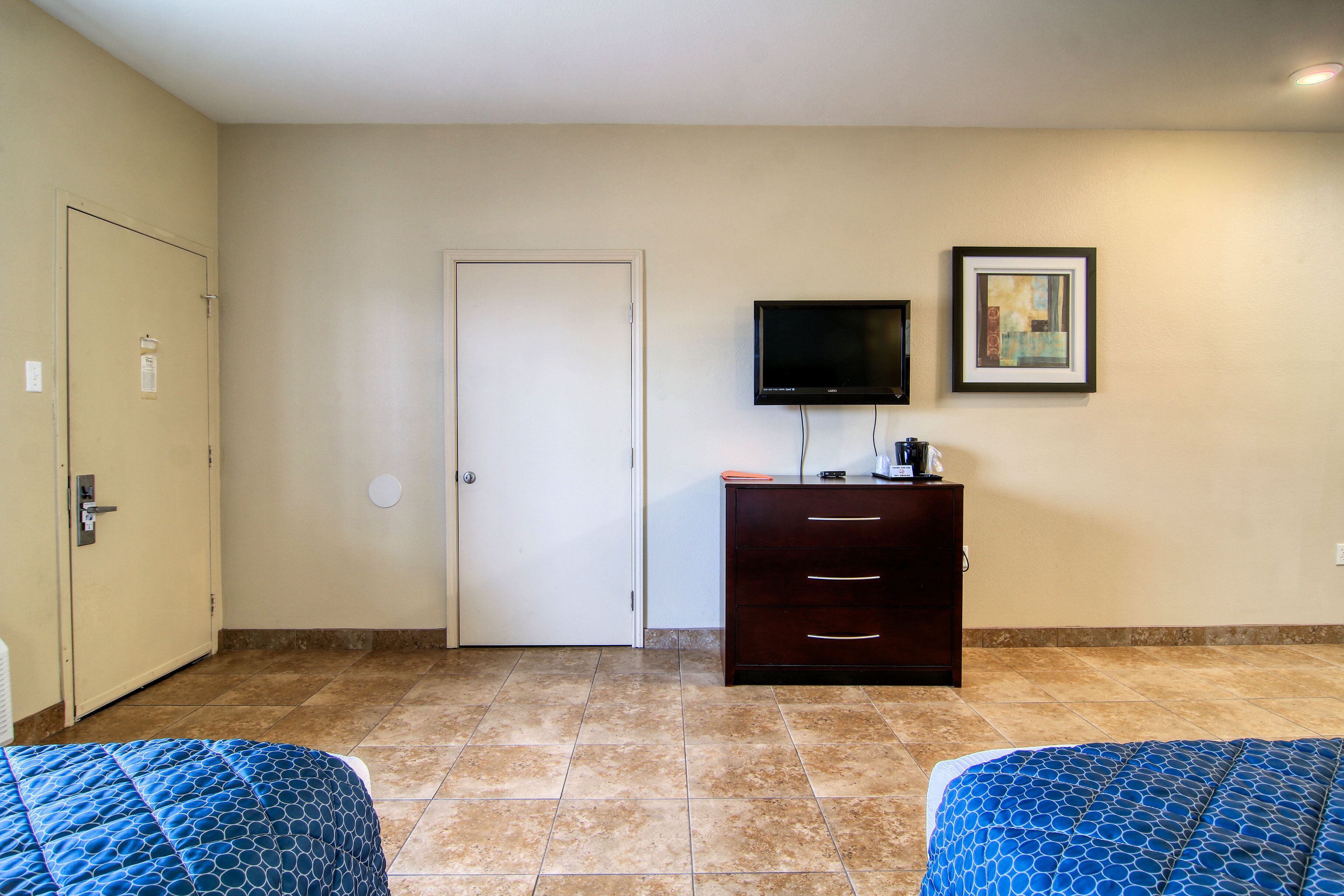 A hotel room with two beds, a TV, a dresser, and a door.
