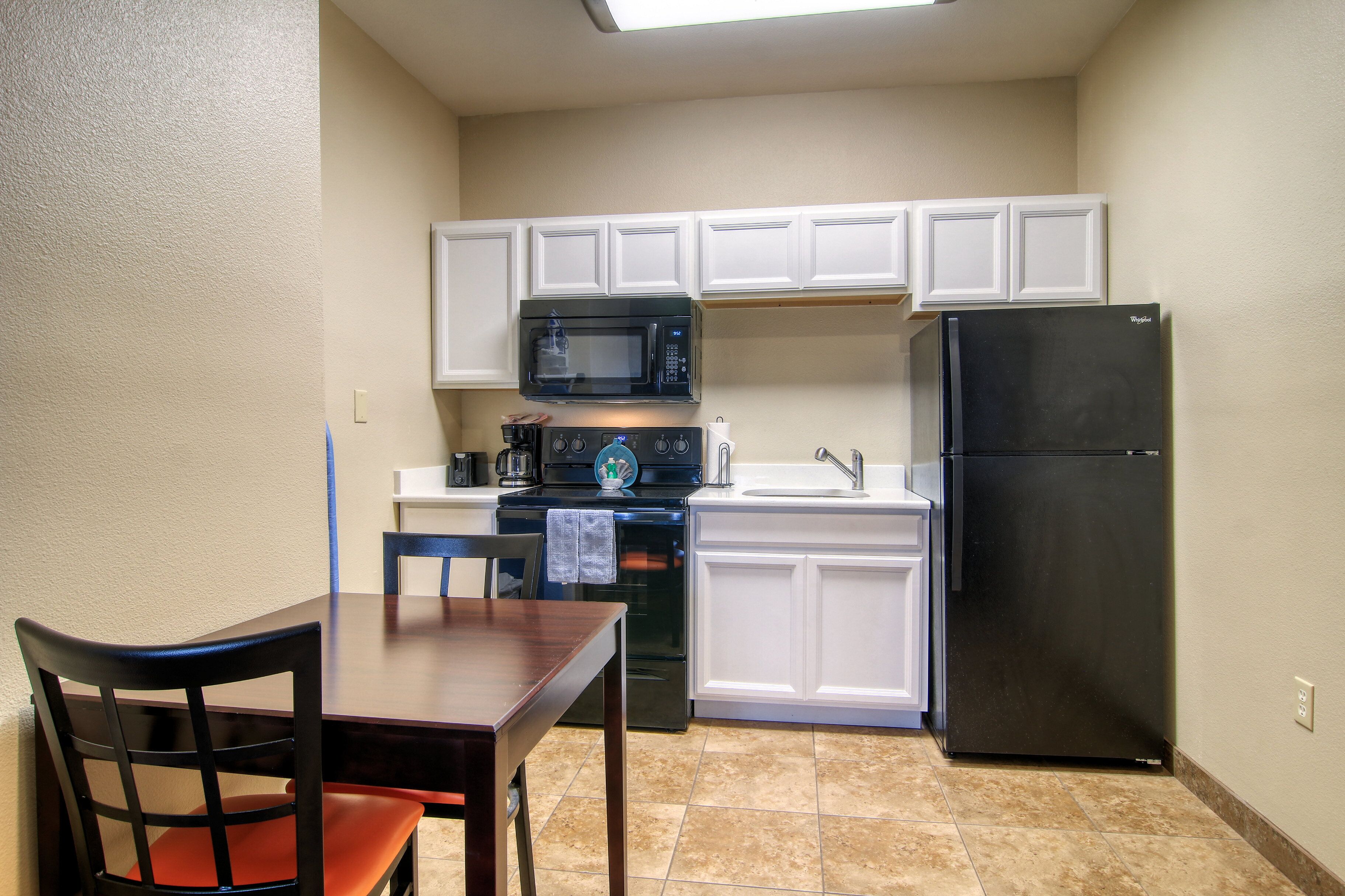 A compact kitchen with white cabinets, a black refrigerator, a microwave, and a stove.