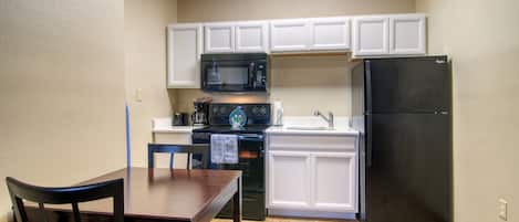 A compact kitchen with white cabinets, a black refrigerator, a microwave, and a stove.