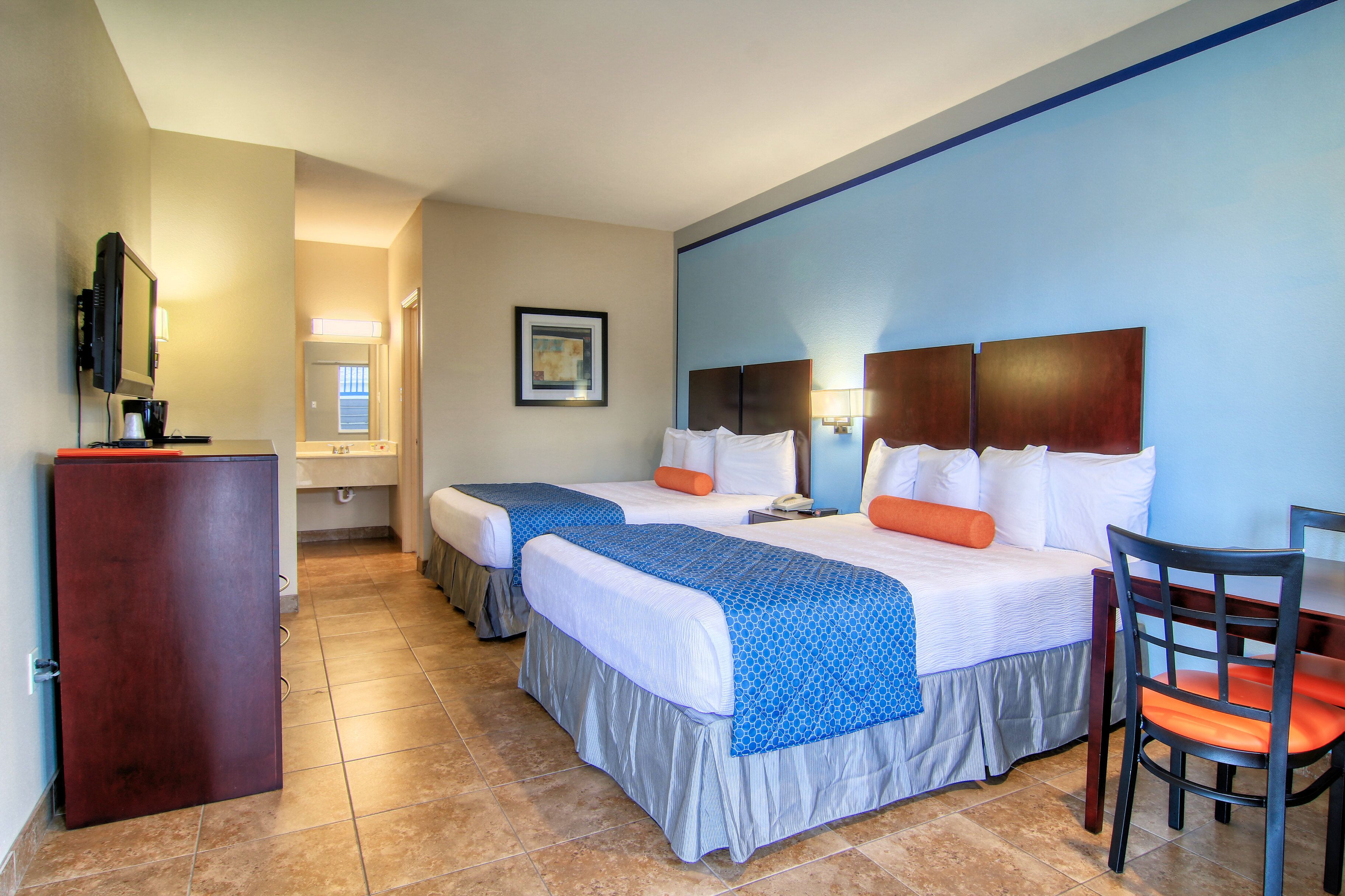 A hotel room with two beds, a desk, a chair, a television, and a framed picture on the wall.