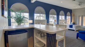 A modern hotel room with a kitchen area, a dining table, and a seating area with a blue sofa.