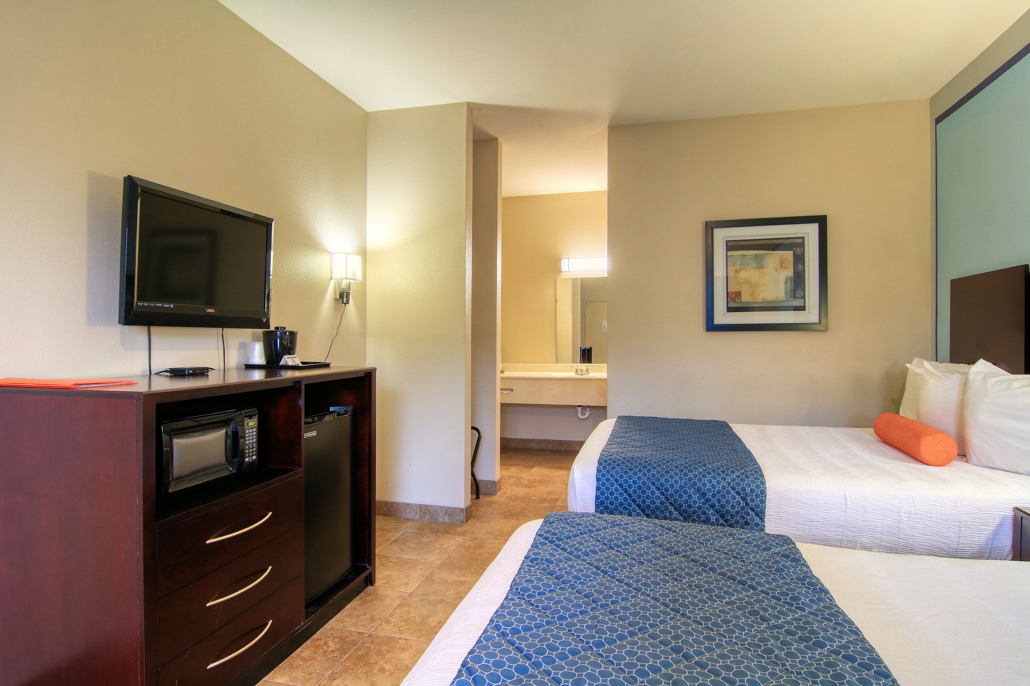 Habitación de hotel con dos camas, televisión, microondas y una pequeña kitchenette.