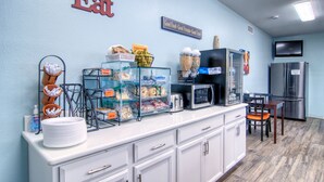 A breakfast bar with food items, a microwave, and a refrigerator. - Alister Square Inn (Port Aransas)