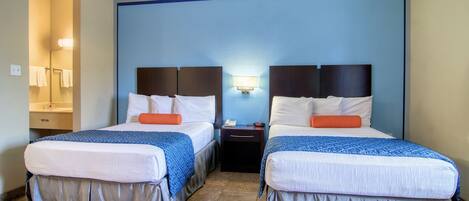 Una habitación de hotel con dos camas, una mesita de noche y una lámpara de pared.
