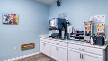 Una cocina con cafetera, microondas y diversos alimentos. Hay un cartel en la pared y un cuadro sobre la encimera.