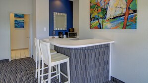 A modern kitchen with a white countertop, a microwave, and a coffee maker. There is a blue wall and a painting of sailboats. - Alister Square Inn (Port Aransas)