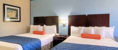 Two double beds with blue and white bedding, a nightstand with a phone and remote, and a framed picture on the wall.