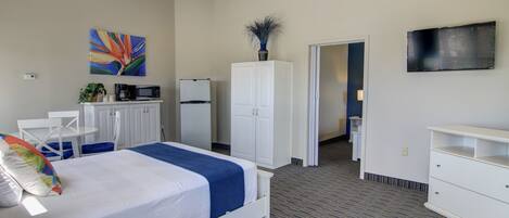 A hotel room with a bed, white wardrobe, a microwave, a refrigerator, a TV, and a painting on the wall.