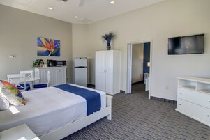 Habitación de hotel con cama, armario blanco, microondas, refrigerador, televisor y un cuadro en la pared.